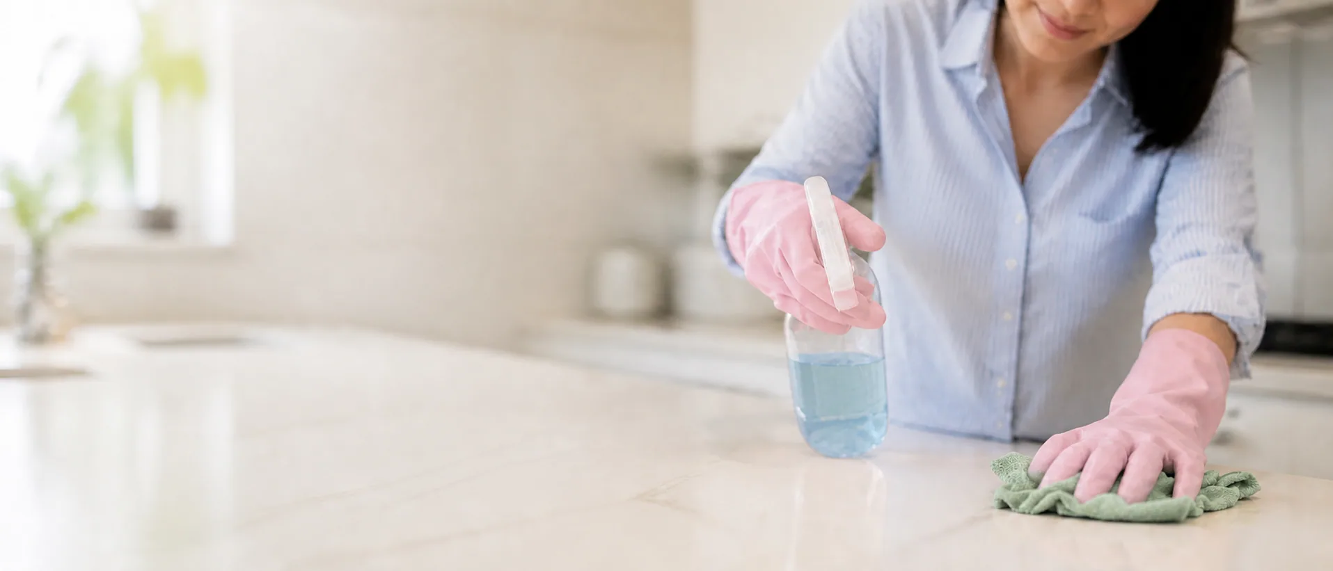 Homeowner cleaning a kitchen countertop with a spray bottle and microfiber cloth